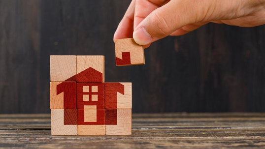 blocks with a house painted on them and someone is placing down the top right corner piece