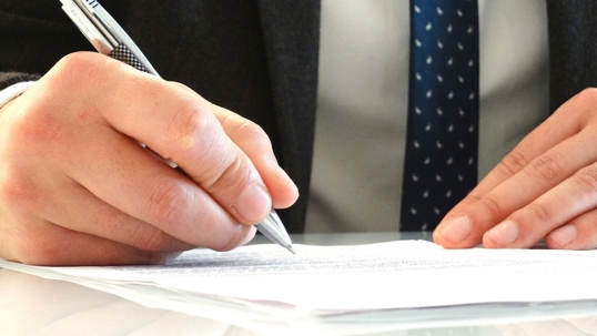 a man in a suit and tie holding a pen above paper